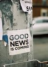 Image of large city street pole with sign, "Good News Is Coming"